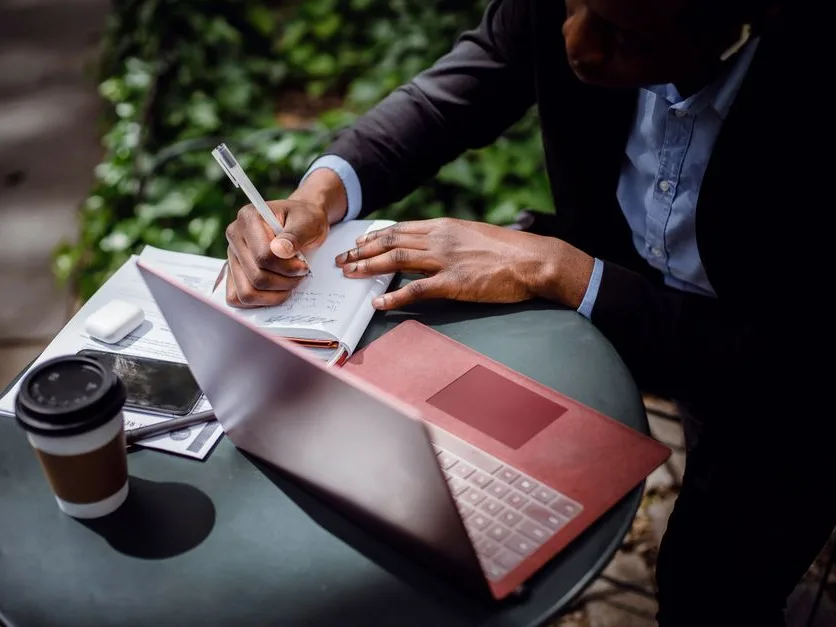 Un journaliste rédige un article à sa table, carnet, ordinateur portable et café à portée de main
